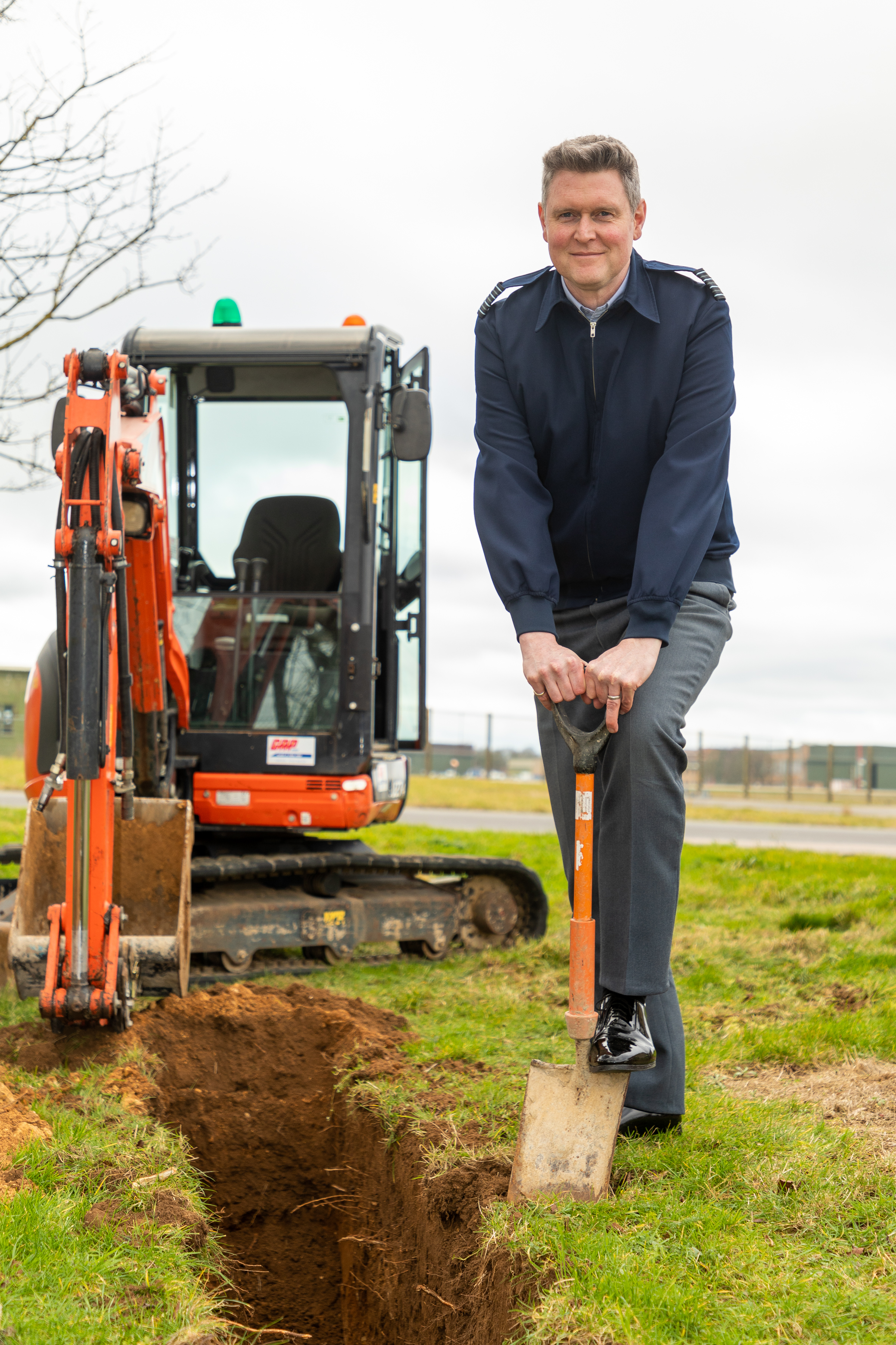 Personnel uses a shovel with digger in background.